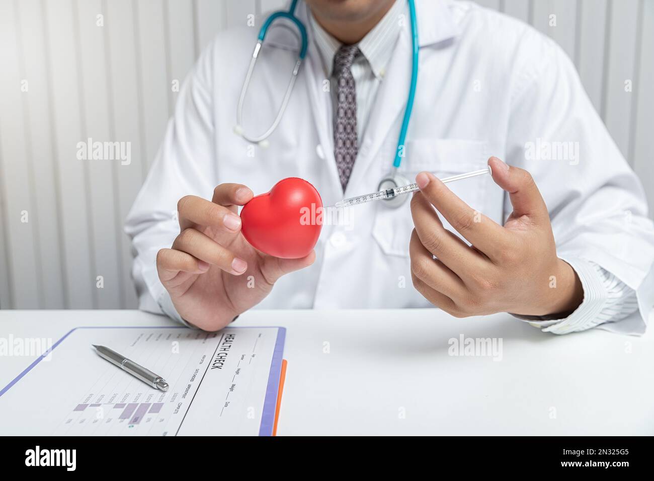 Doctor inject syringe with needle into toy red heart ball. Heart health ...