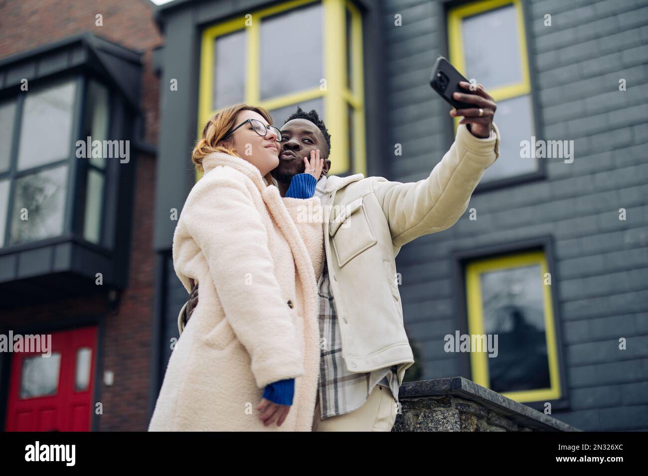 Young interracial couple takes a selfie together on street against background of houses. Concept of love relationships and unity between different hum Stock Photo