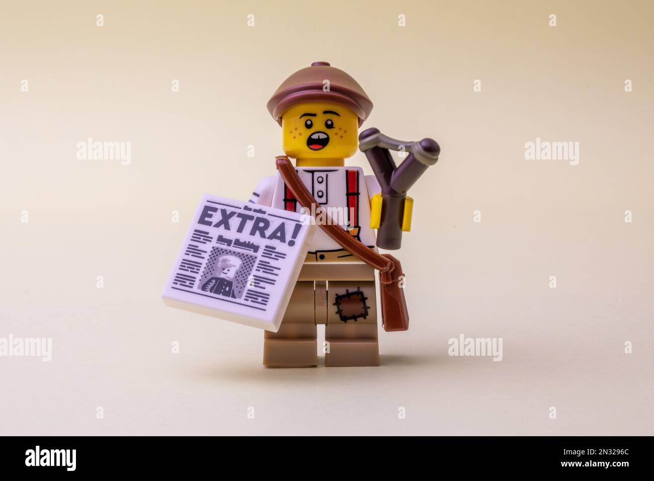 A LEGO minifigure toy holding newspaper and slingshot on pastel