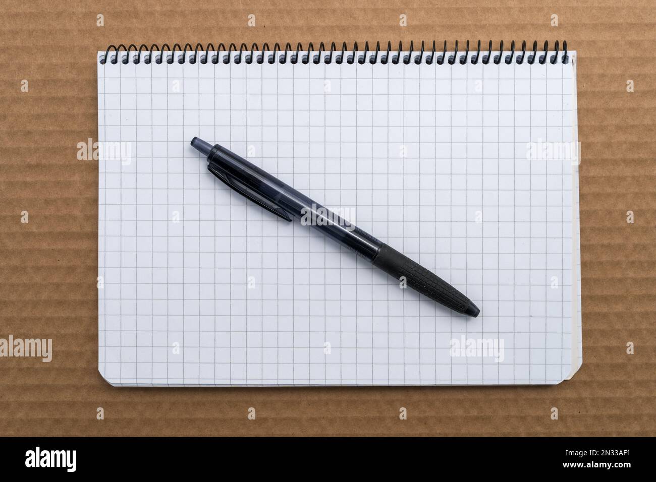 Graph paper spiral Notebook with black ballpoint pen on top of brown cardboard, top view. Stock Photo