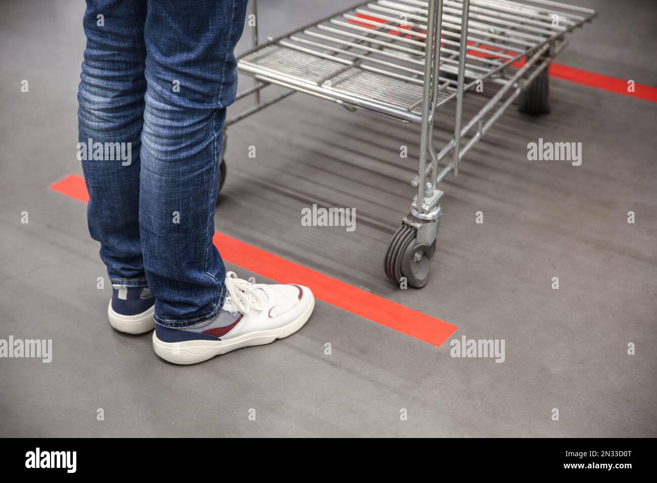 Person with shopping cart standing behind taped floor marking in store for social distance, closeup. Preventive measure during coronavirus pandemic Stock Photo
