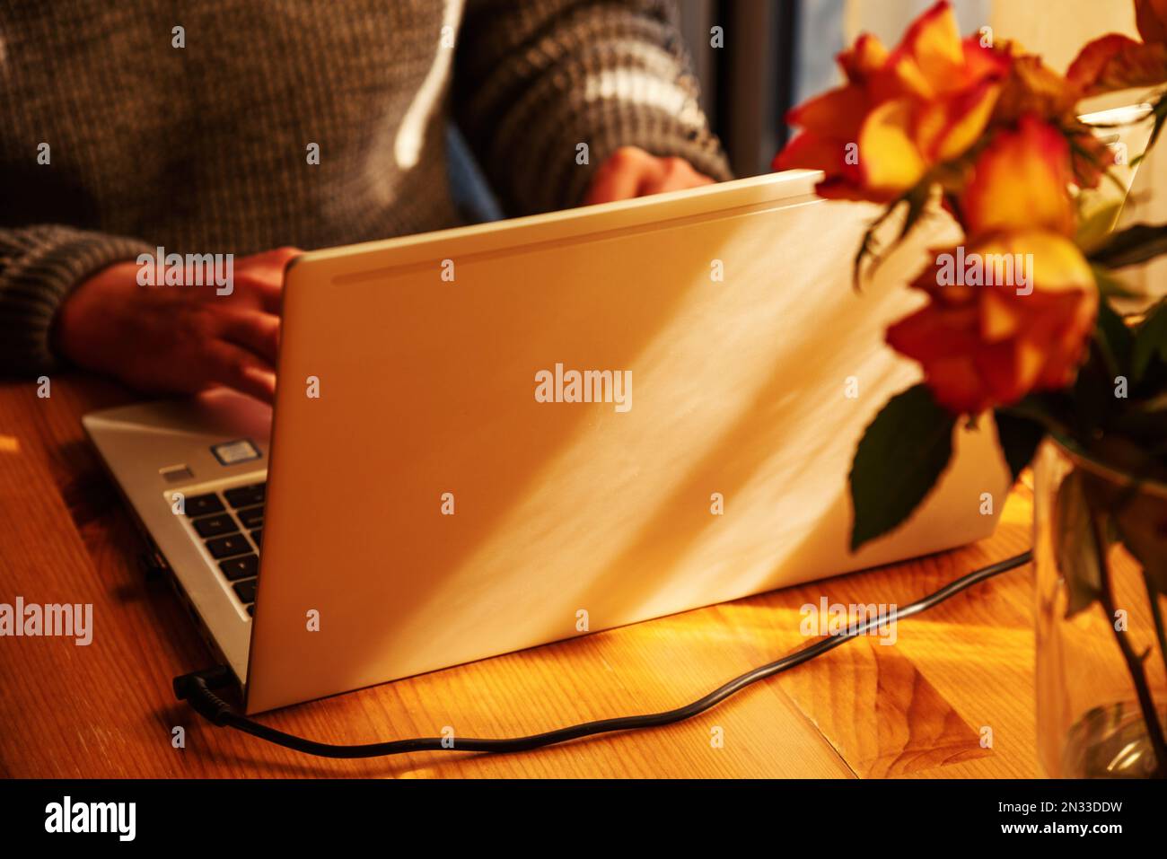 Man working from home at simple candid workplace with laptop computer in sunset light. Remote working from home in comfortable working environment. Stock Photo