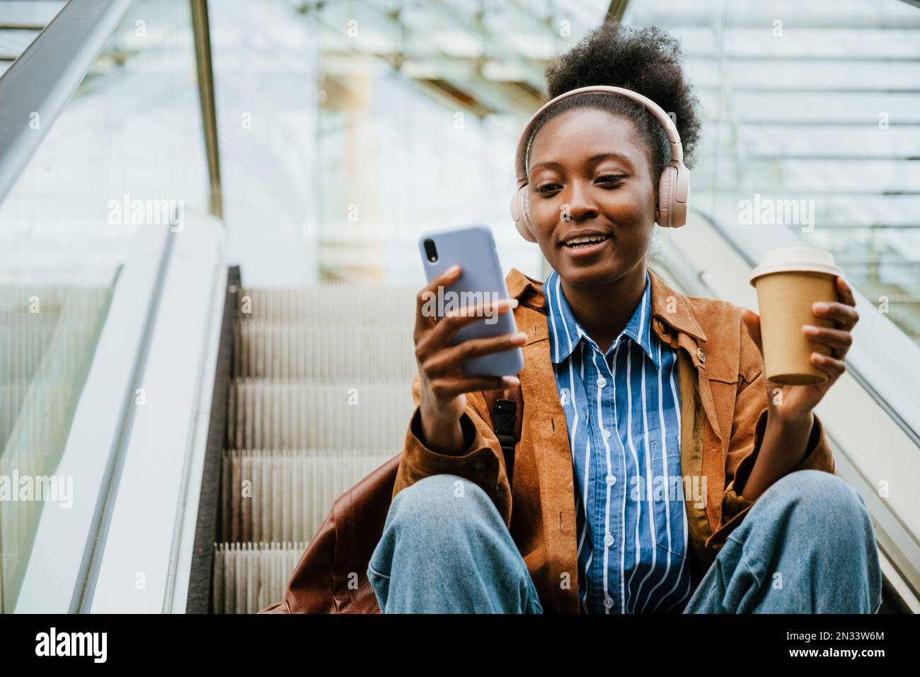 Young african american woman using cellphone and drinking coffee while ...