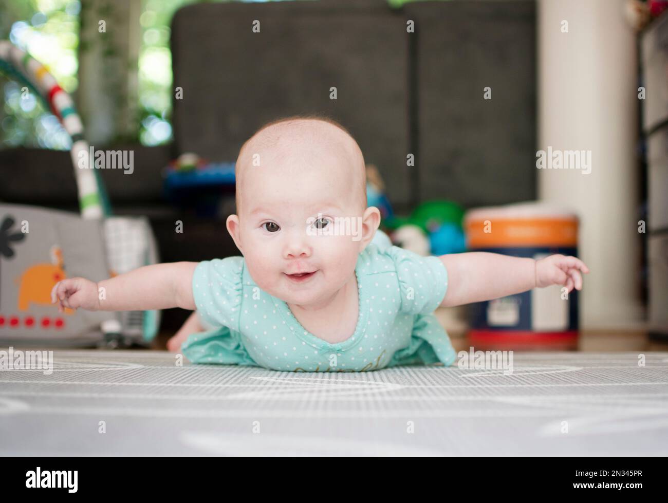 Infant baby girl on the floor during tummy time with her arms up like