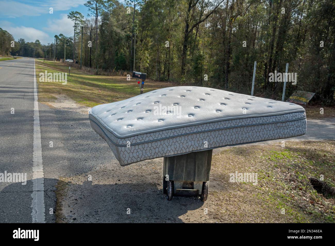 Discarded mattress sits atop garbage can next to a highway in North Central Florida. Stock Photo