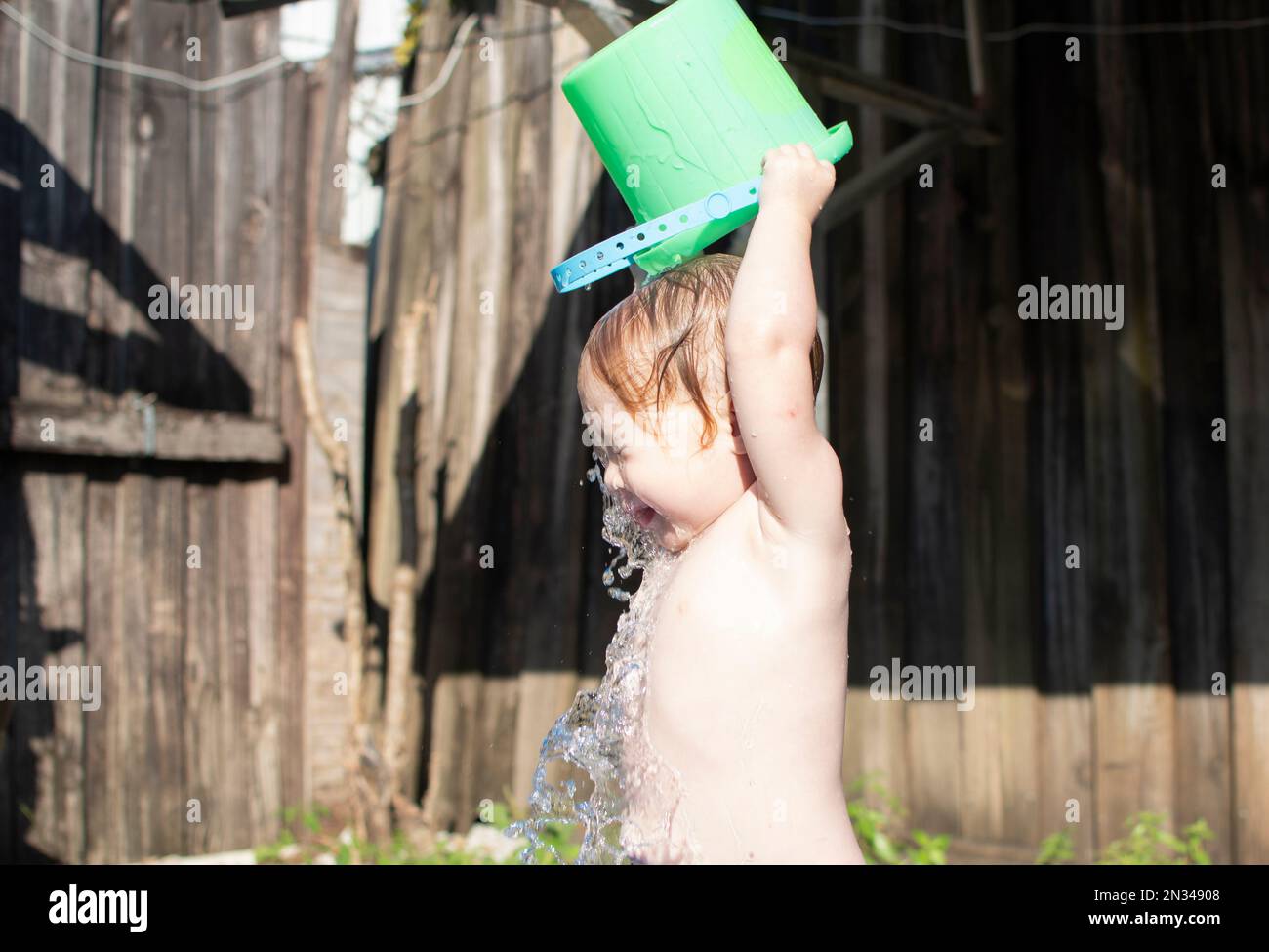 Caucasian toddler girl pouring water on her head from the green bucket