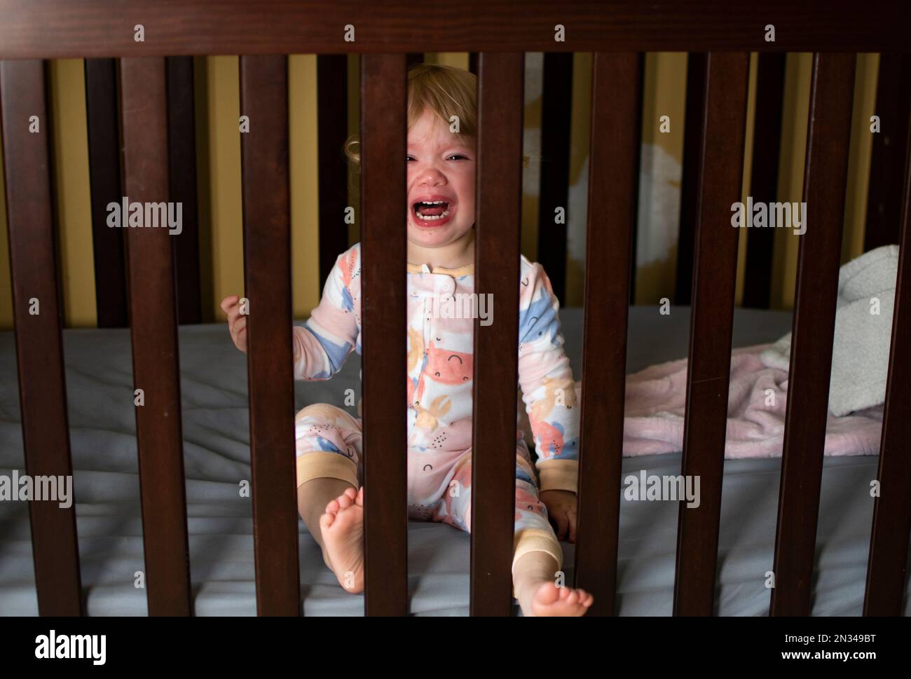 Caucasian baby girl crying in the crib in her pajamas. Sad Sick child. Teething child Stock Photo