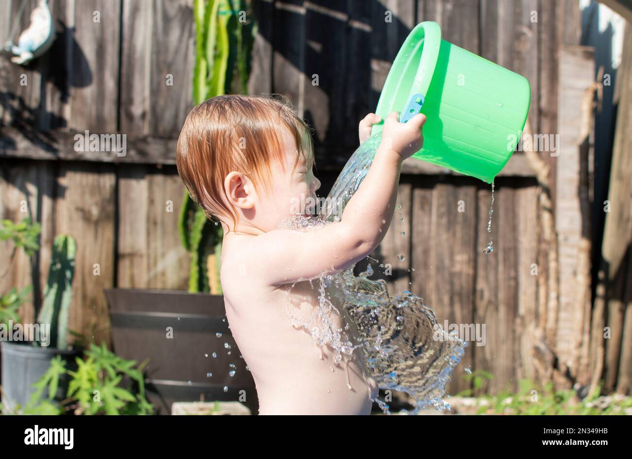 Caucasian toddler girl pouring water on her head from the green bucket