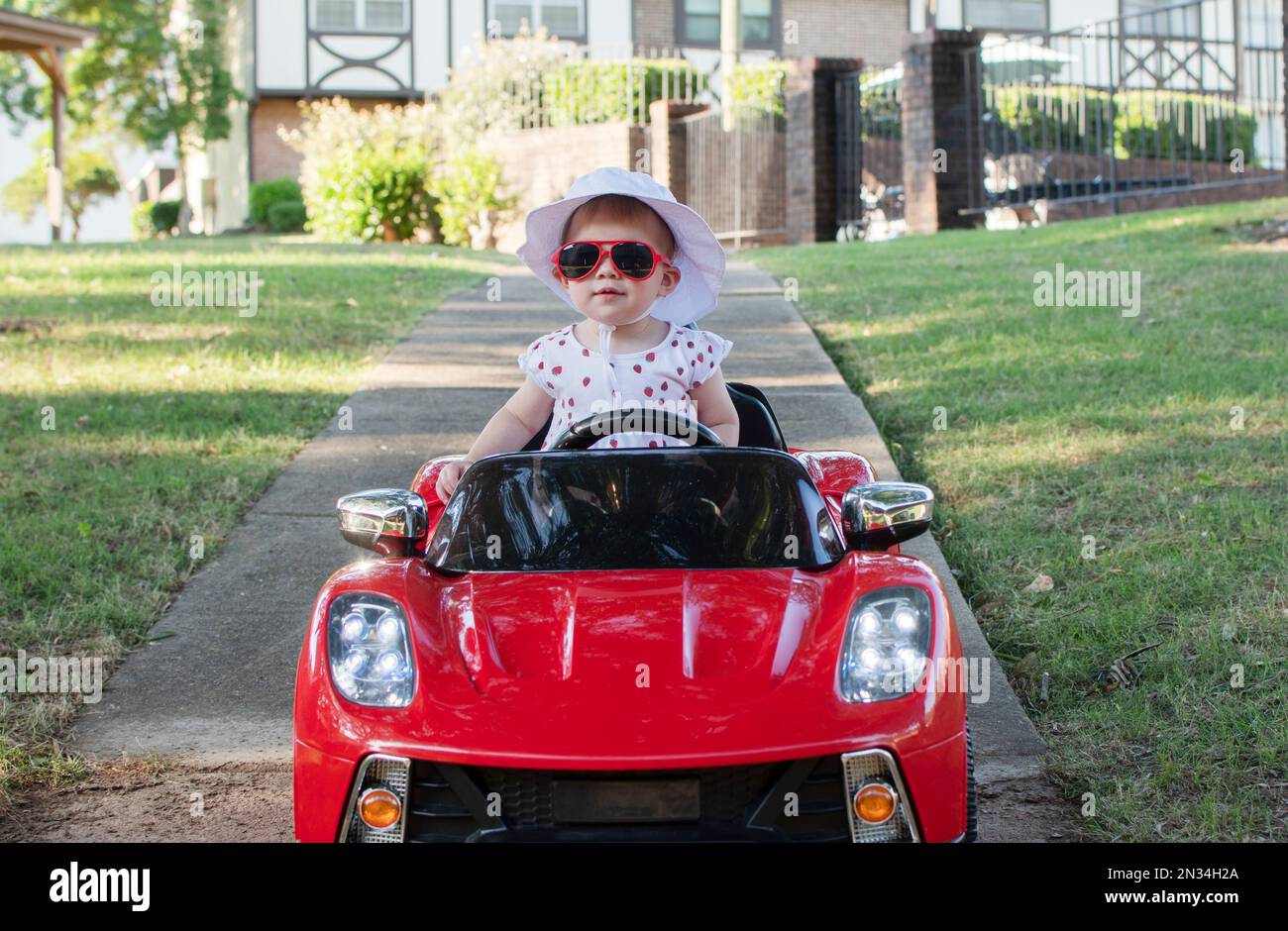 Caucasian baby in white hat riding in an electric convertible red sport car. child driving a car on a summer day Stock Photo