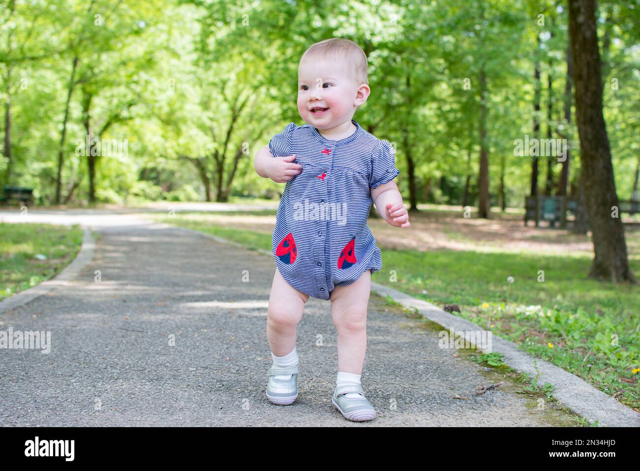 Cute caucasian baby taking first steps in the park. Toddler walking Stock Photo