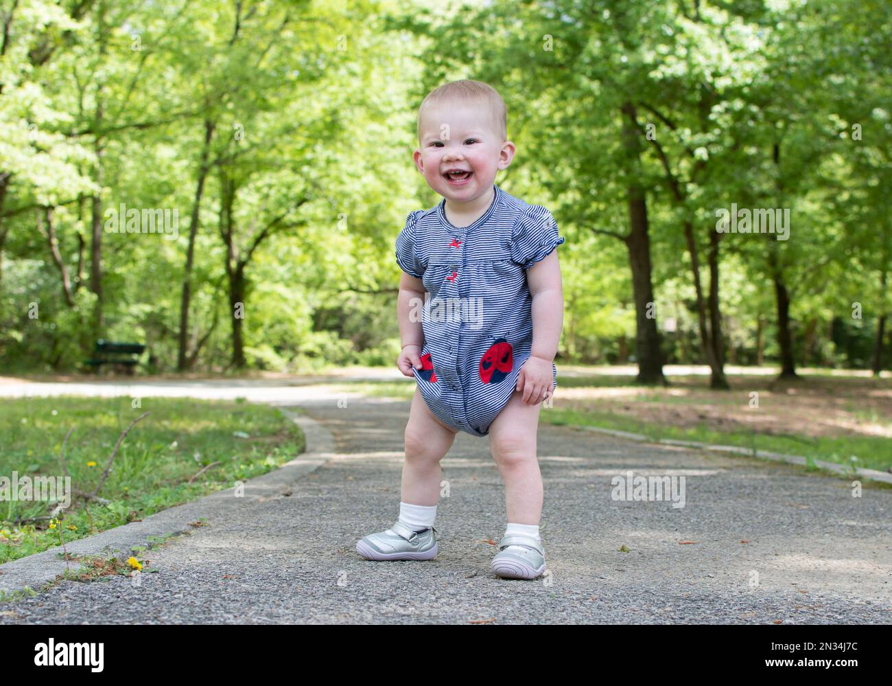 Cute caucasian baby taking first steps in the park. Toddler walking Stock Photo