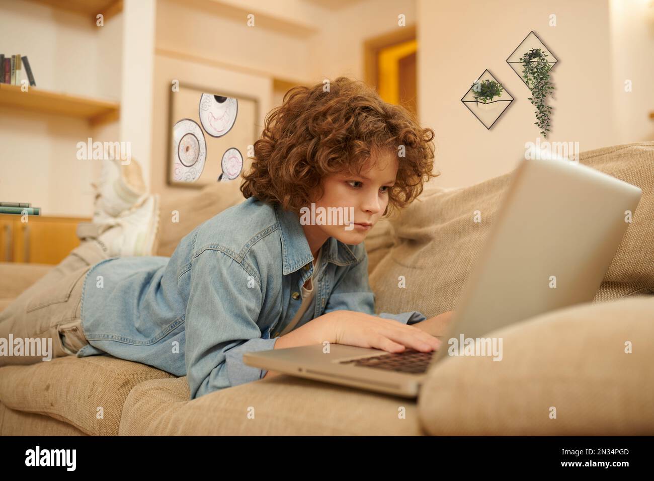 A curly-haired boy spending time on internet and looking involved Stock Photo