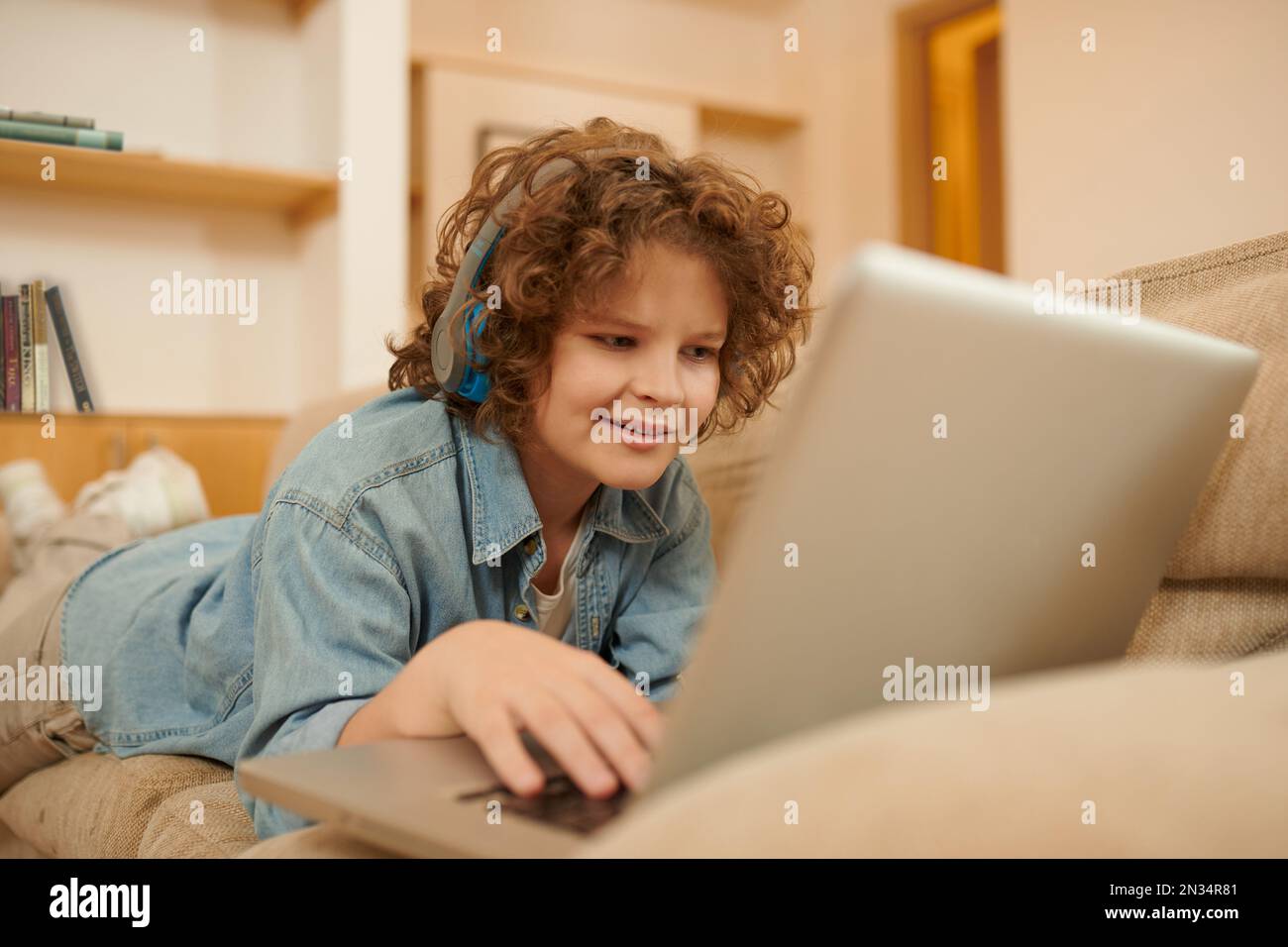 A curly-haired boy spending time on internet and looking involved Stock Photo
