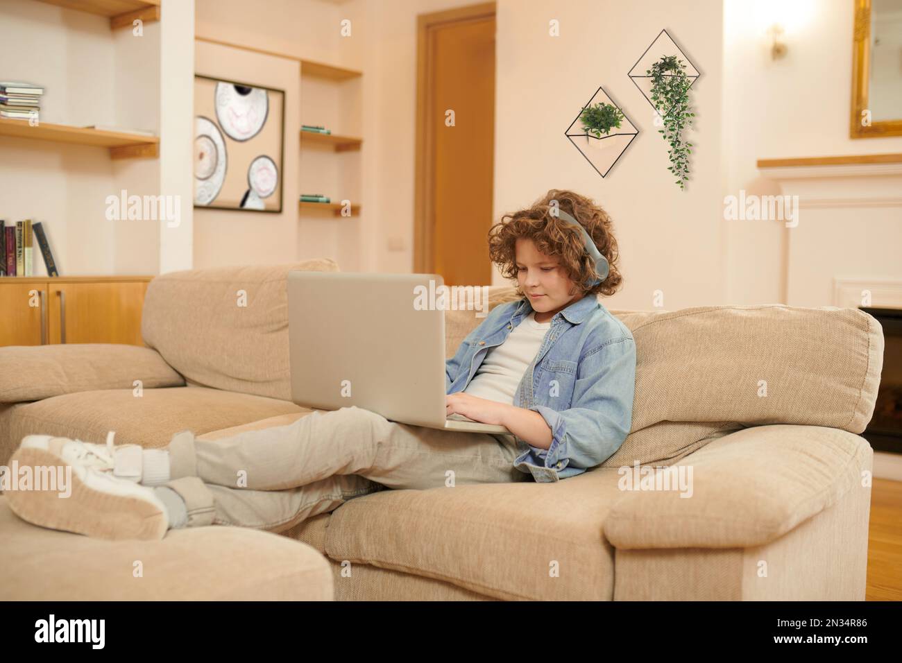 A curly-haired boy spending time on internet and looking involved Stock Photo