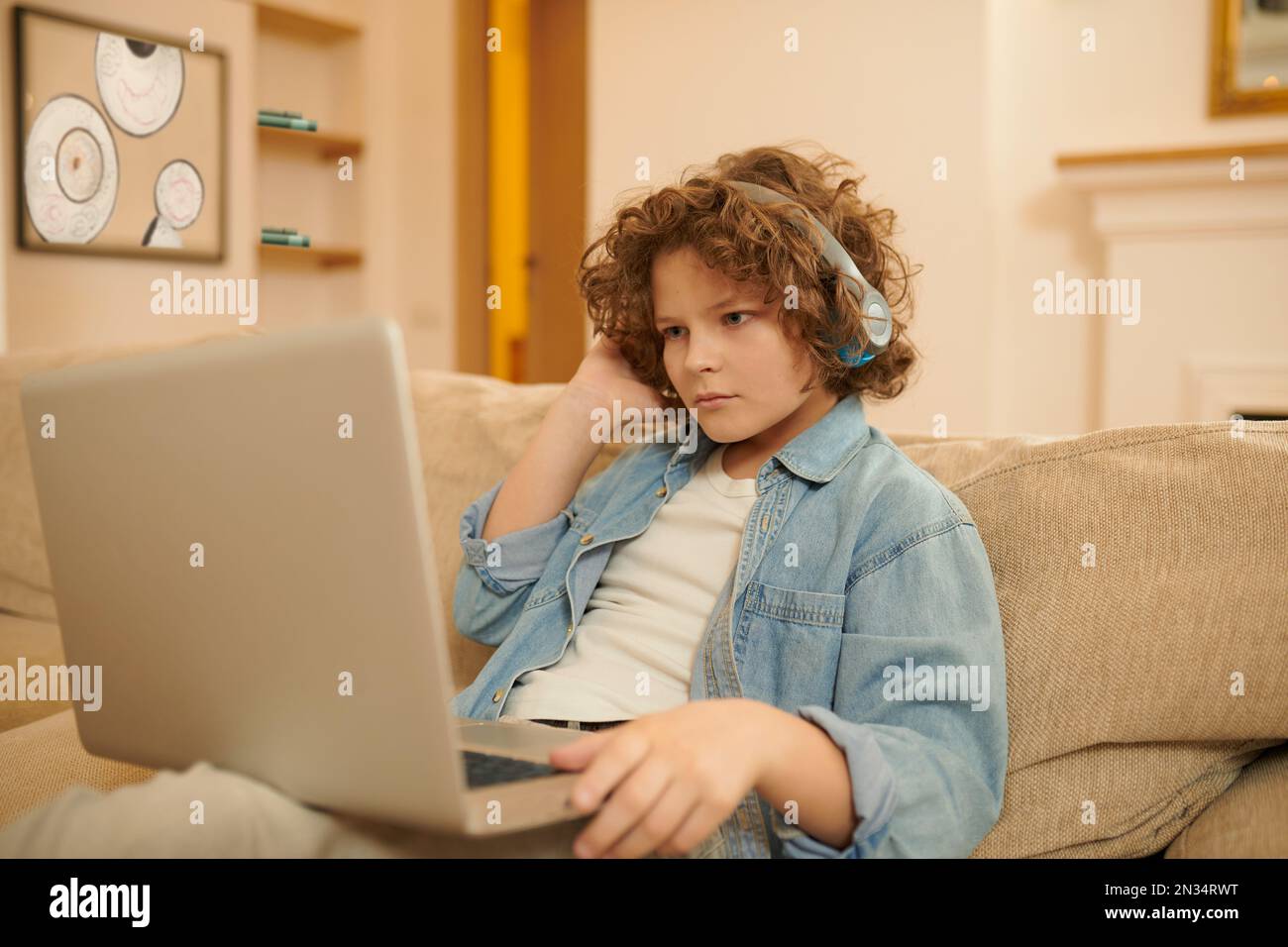 A curly-haired boy spending time on internet and looking involved Stock Photo