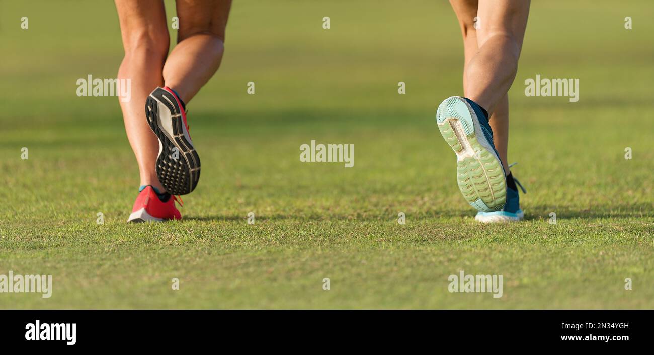 Couple runners athletes feet running on grass. Female fitness sunlight