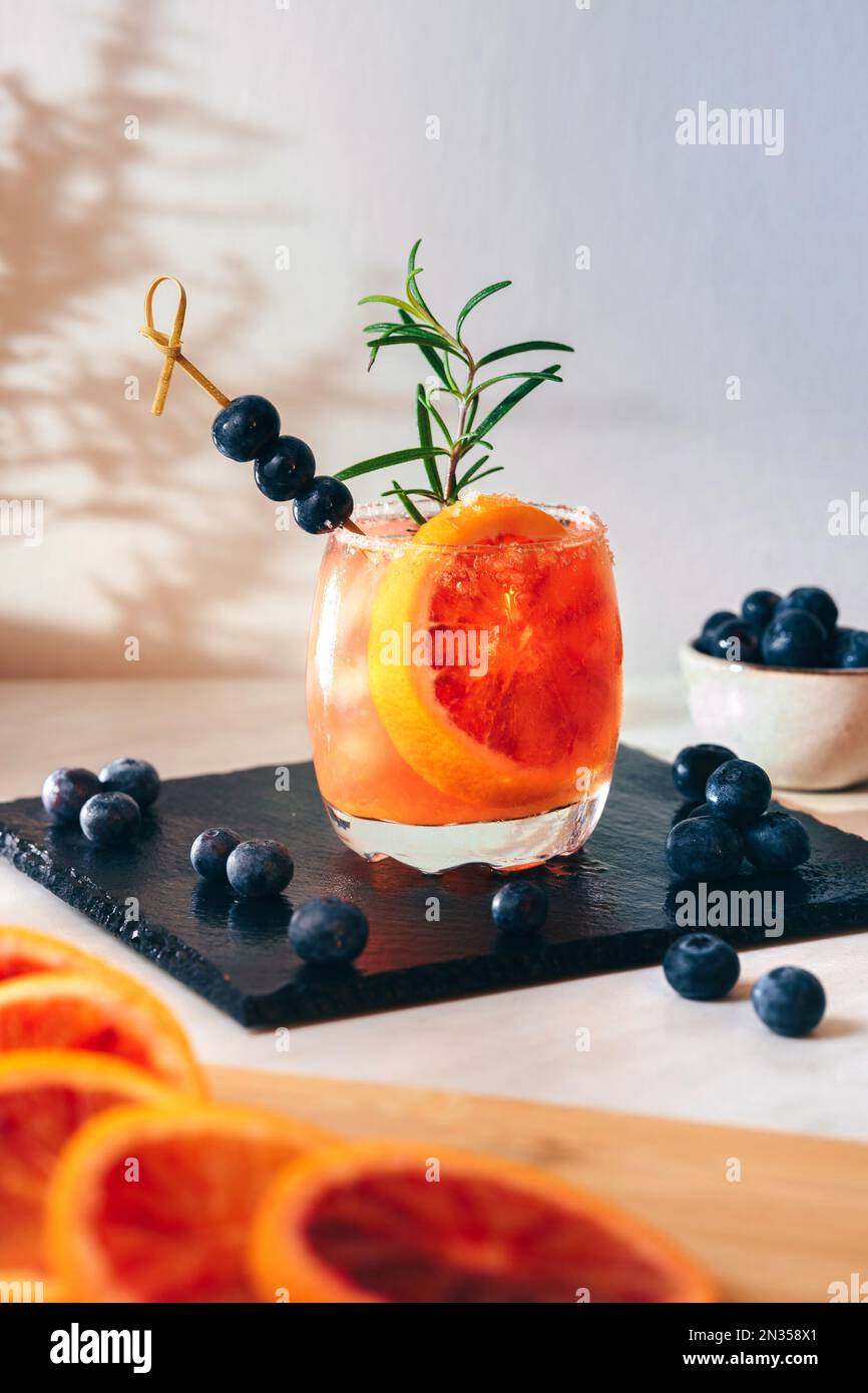 a cocktail with ice, bluberries, a slice of fresh orange, a rounded glass, with rosemary and fresh fruit. Stock Photo