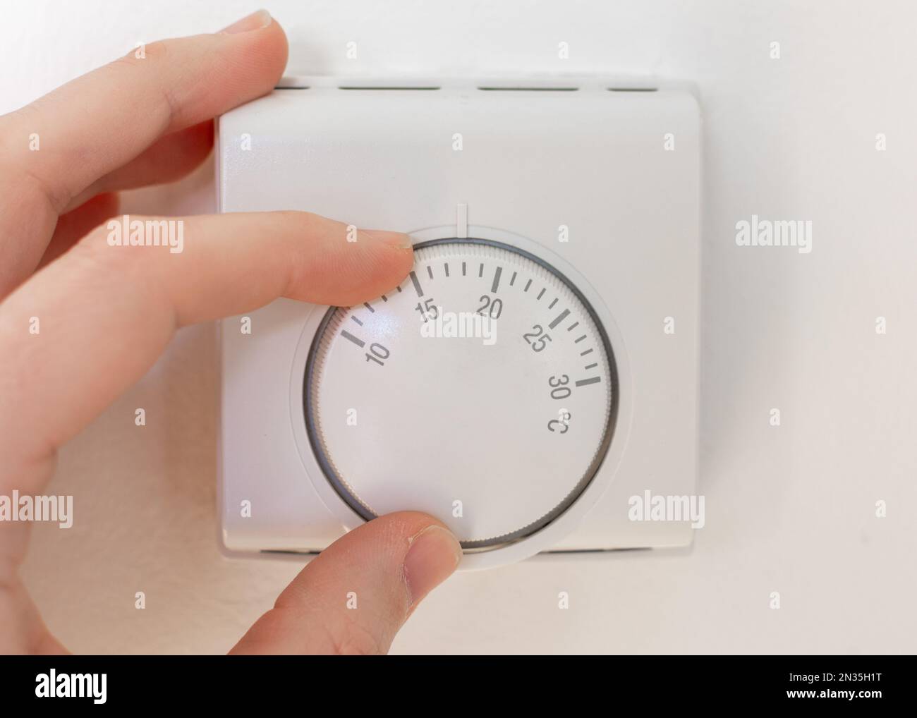 A man turning the thermostat dial, heating and cost of energy concept