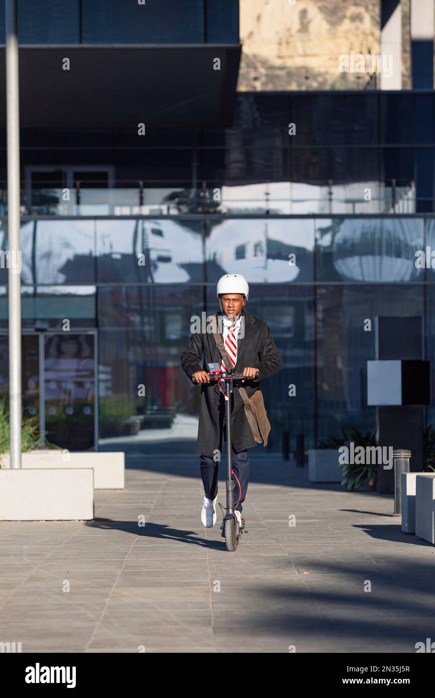 Latin businessman riding electric scooter between office buildings