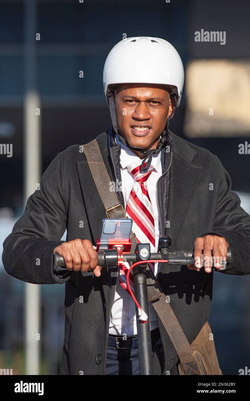 Young businessman in a suit riding an electric scooter looking at