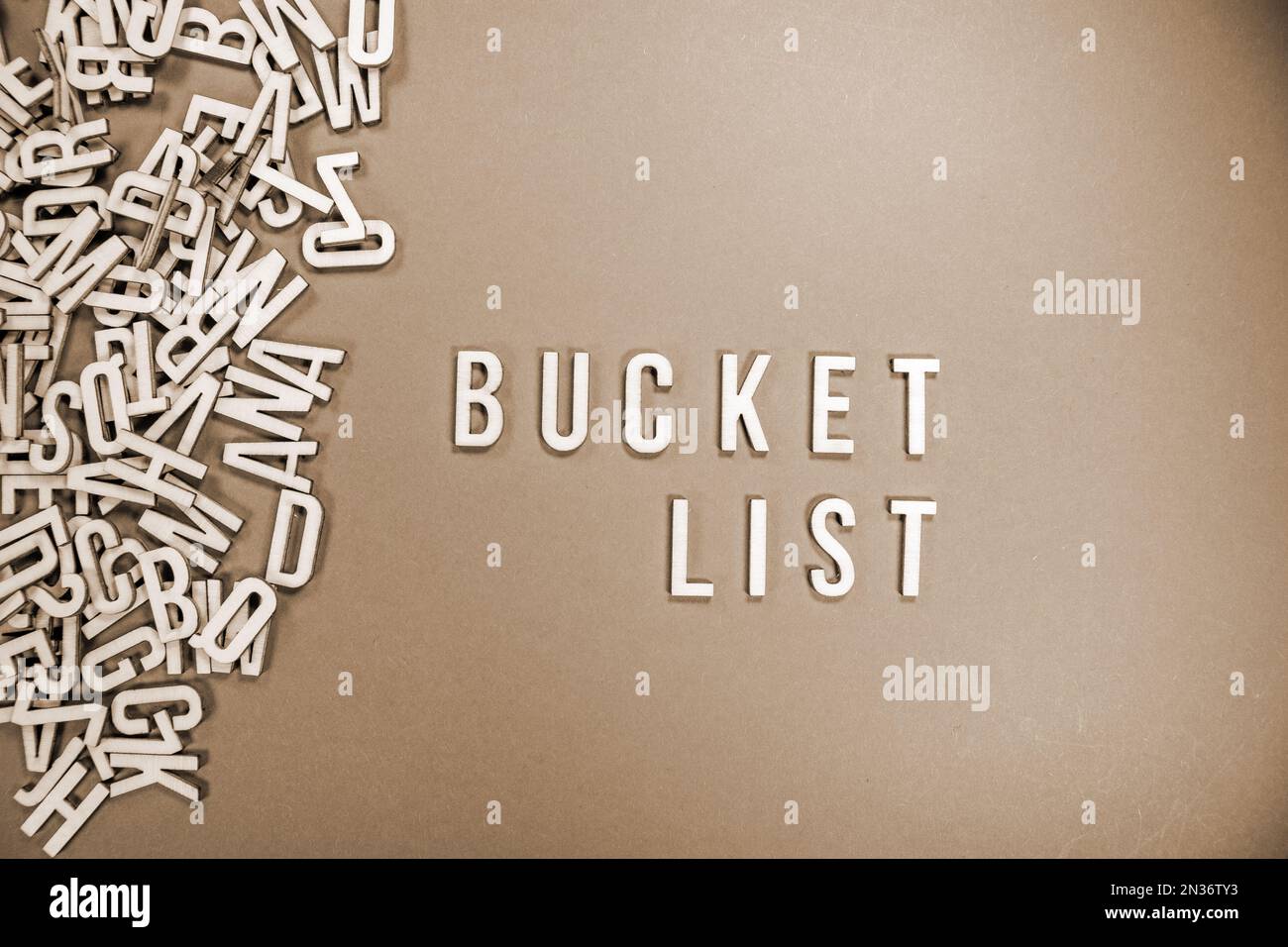 BUCKET LIST in wooden English language capital letters spilling from a pile of letters sepia