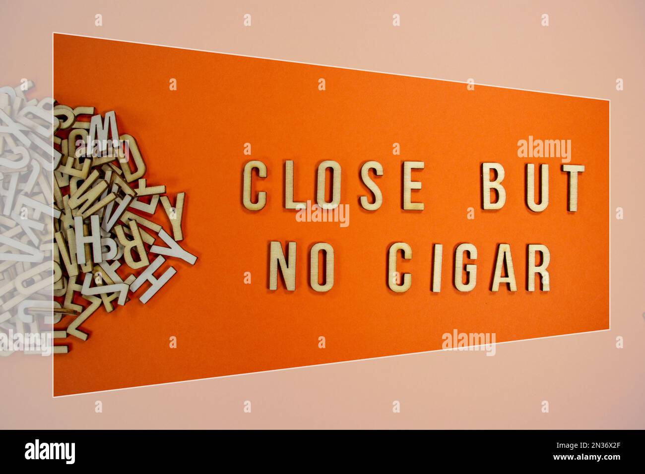 CLOSE BUT NO CIGAR in wooden English language capital letters spilling from a pile of letters on a orange background framed Stock Photo
