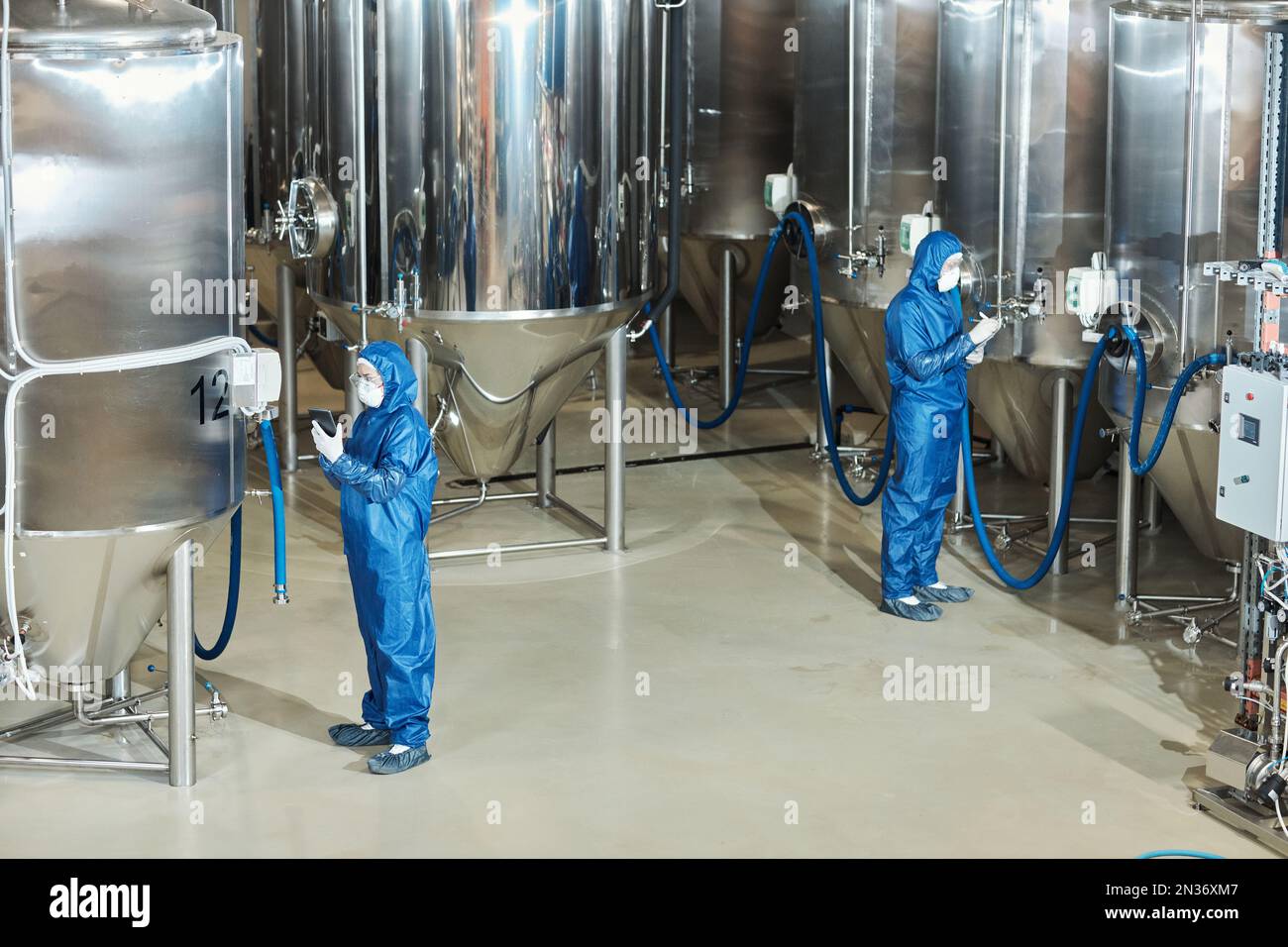 Wide angle view at factory workshop with two workers operating storage tanks, copy space Stock Photo