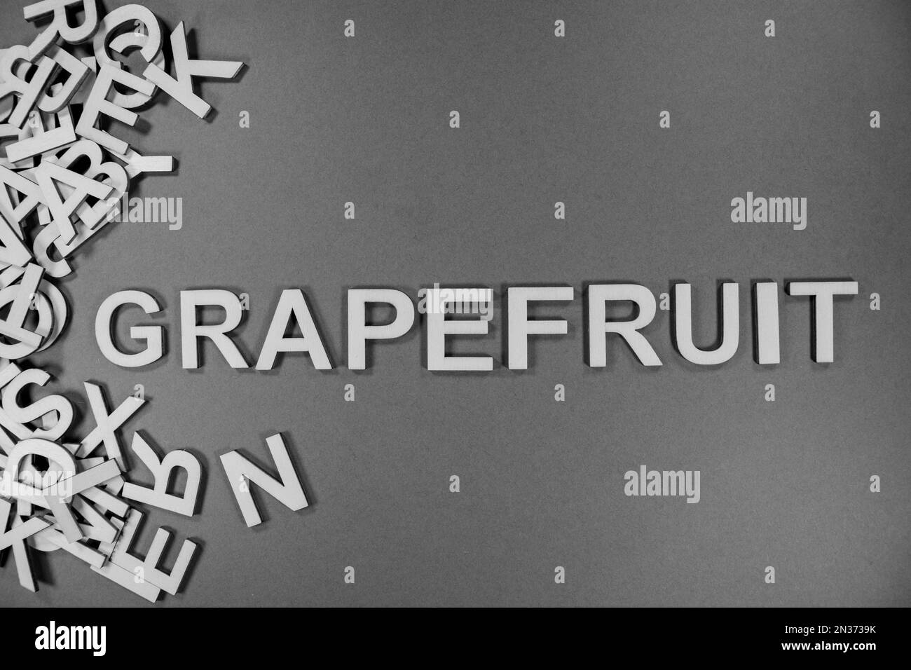 GRAPEFRUIT in wooden English language capital letters spilling from a pile of letters in black and white Stock Photo