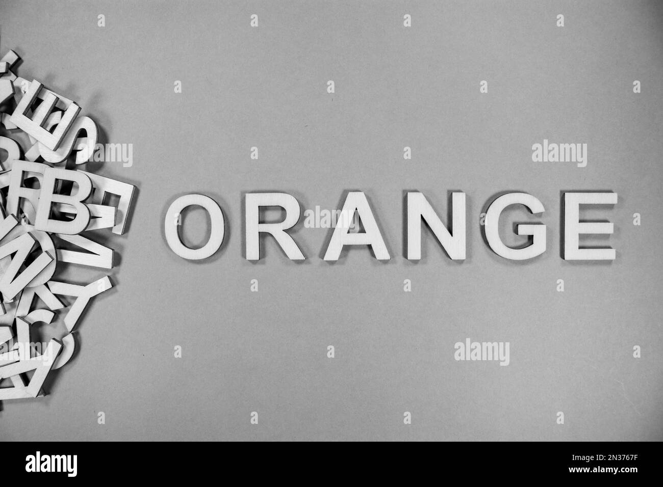 ORANGE in wooden English language capital letters spilling from a pile of letters in black and white Stock Photo