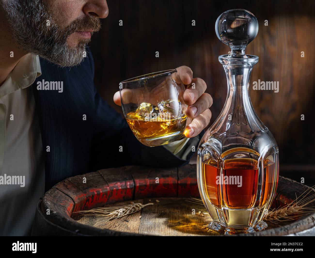 Whisky tasting. Man sits in front of a barrel with a decanter and a glass of whiskey. Stock Photo