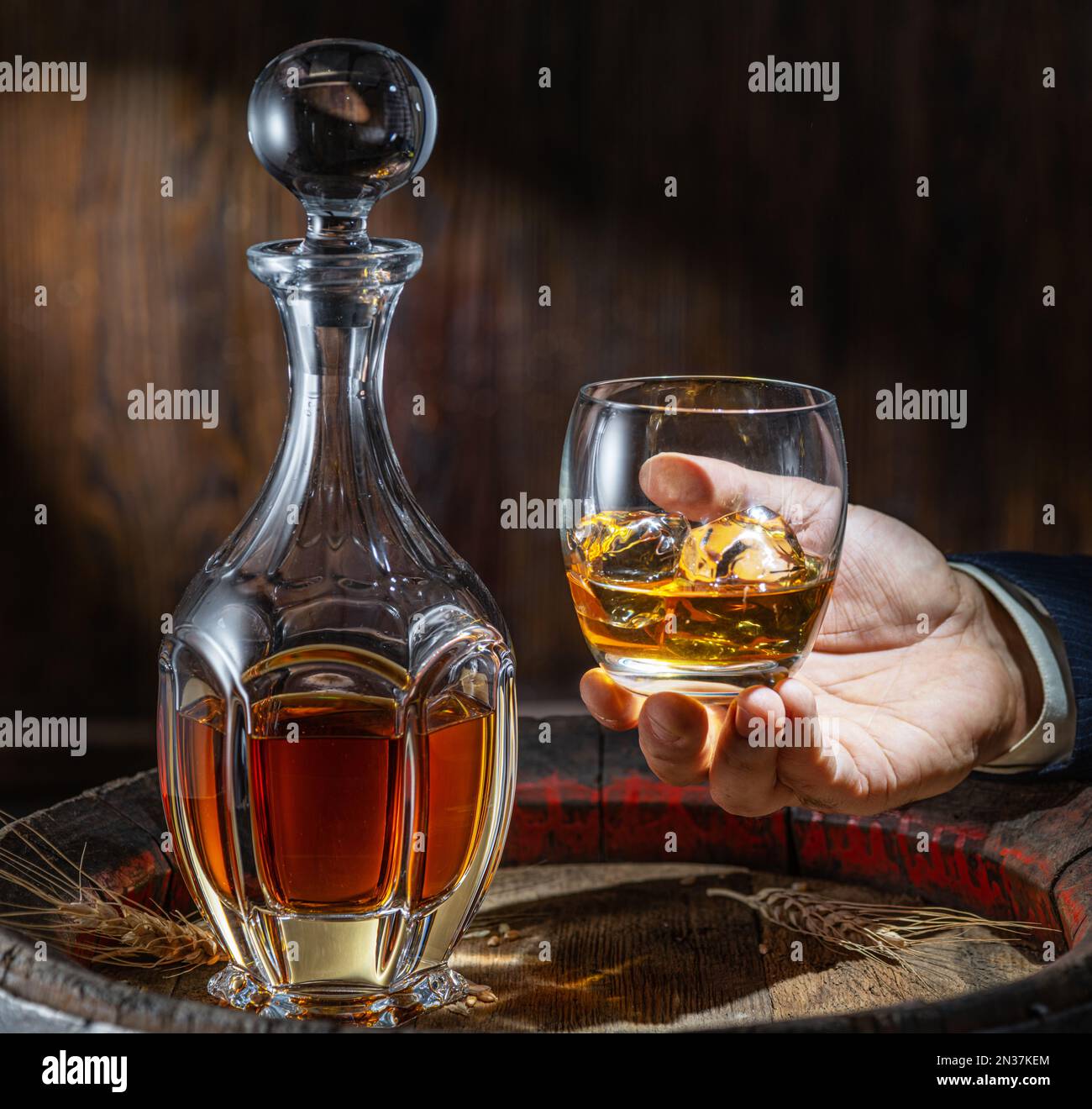 Whisky tasting. Man sits in front of a barrel with a decanter and a glass of whiskey. Stock Photo