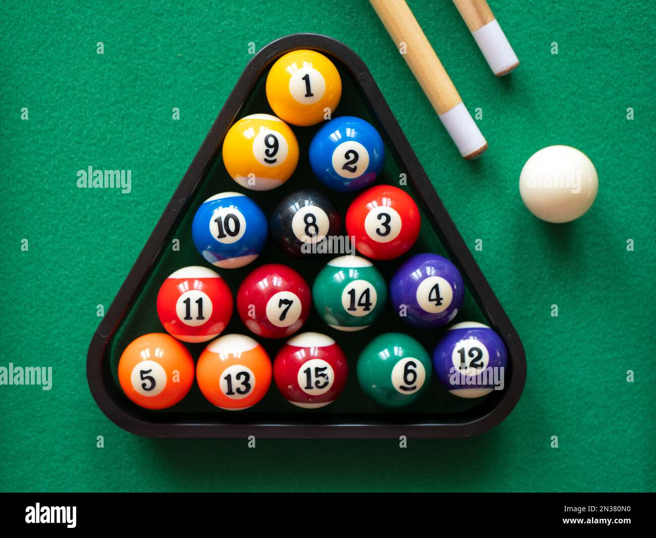 Spots and stripes balls in triangle, cue ball and two cues on the green table, selective focus. Mini billiard, pool or snooker Stock Photo