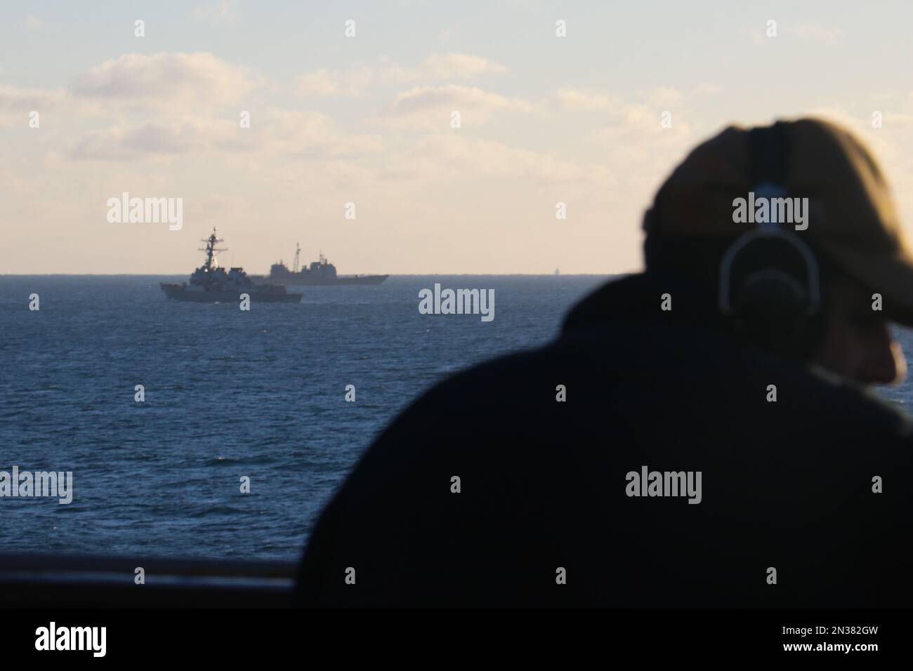 ATLANTIC OCEAN (Feb. 4, 2023) Seaman Rafael Mendez stands watch aboard the dock landing ship USS Carter Hall (LSD 50) while the guided-missile destroyer USS Oscar Austin (DDG 79) and the guided-missile cruiser USS Philippine Sea (CG 58) transit alongside debris from a high-altitude surveillance balloon. Carter Hall is the lead ship in debris recovery efforts led by the Navy, in joint partnership with the U.S. Coast Guard, with multiple units in support of the effort, including ships, aircraft, and an Explosive Ordnance Disposal mobile diving and salvage unit. At the direction of the President Stock Photo