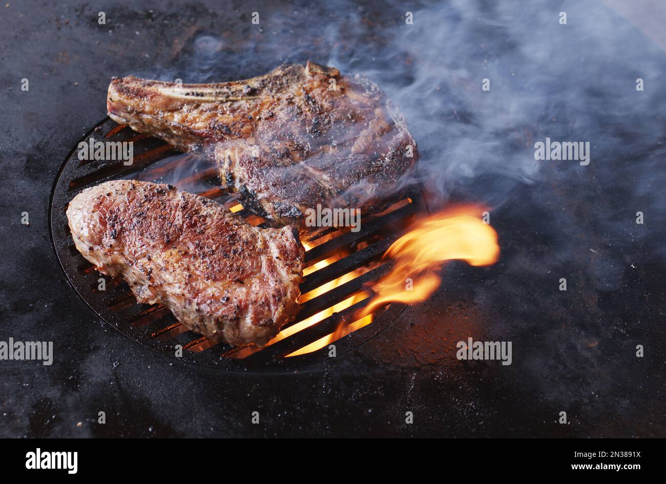 Two steaming beef steaks on grill cooking process. Top view Stock