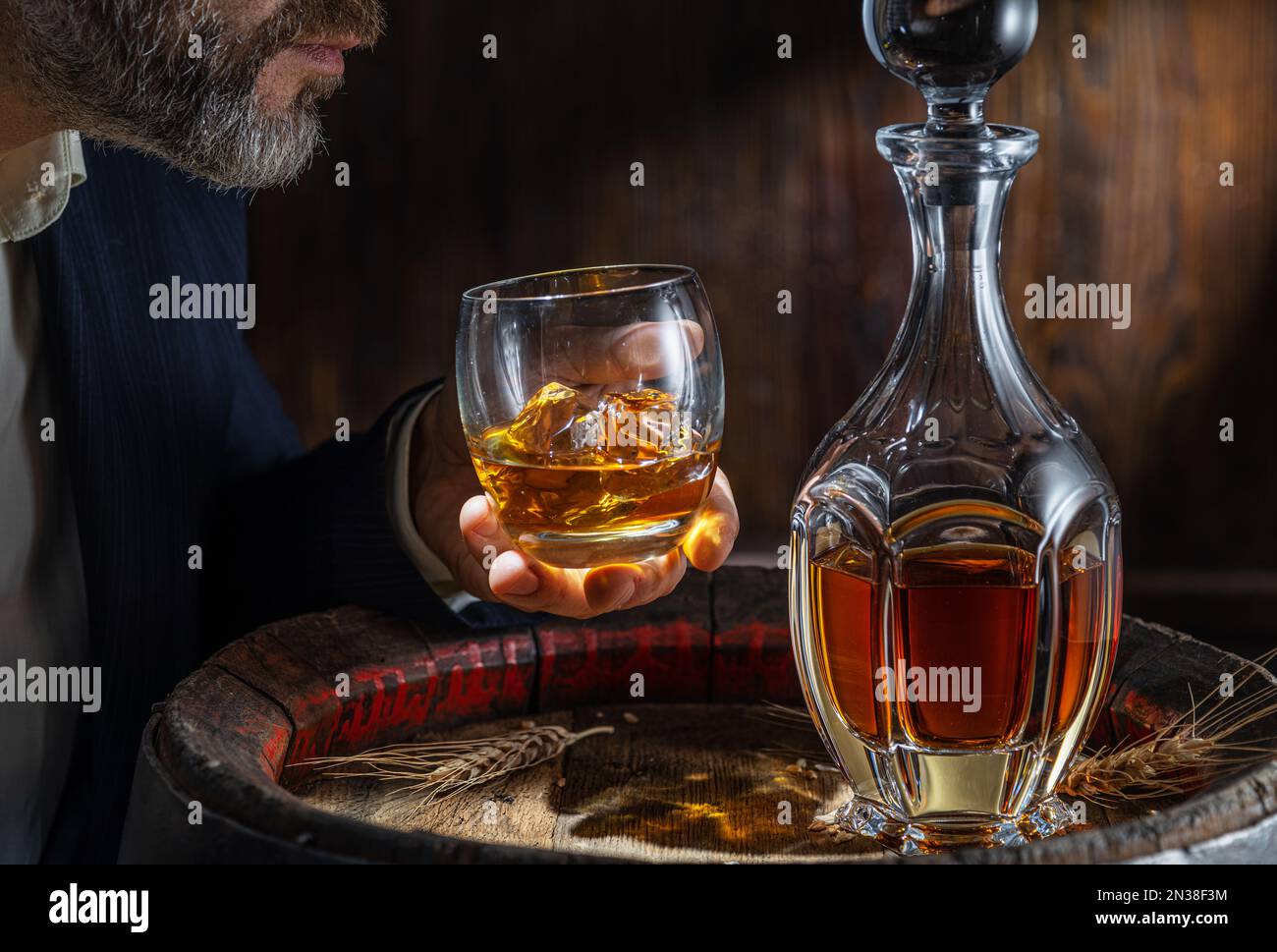 Whisky tasting. Man sits in front of a barrel with a decanter and a glass of whiskey. Stock Photo