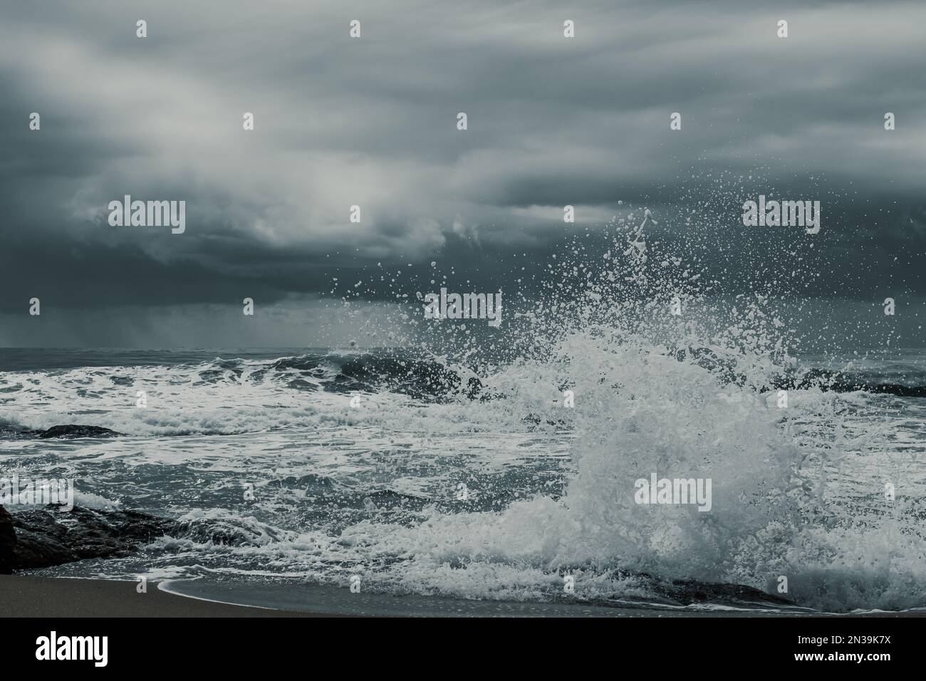 The ocean waves crashing on the beach against a cloudy sky Stock Photo ...