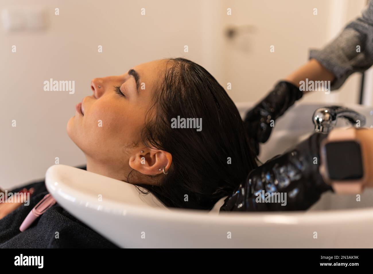 Side view of calm female client lying in sink with closed eyes while getting hair care procedure in salon Stock Photo