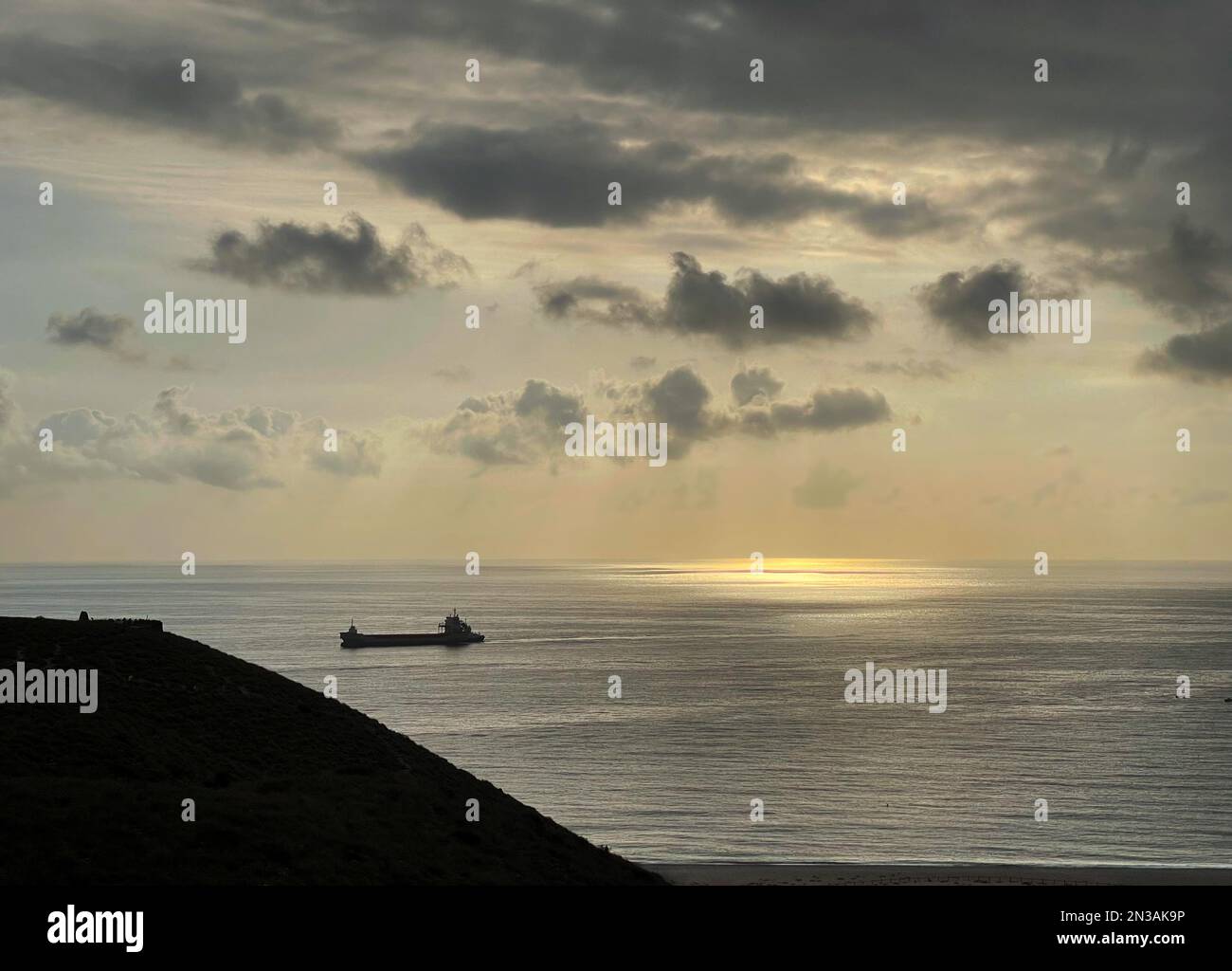 A ship passing on calm sea surface during a mild sunset with cloudscape ...