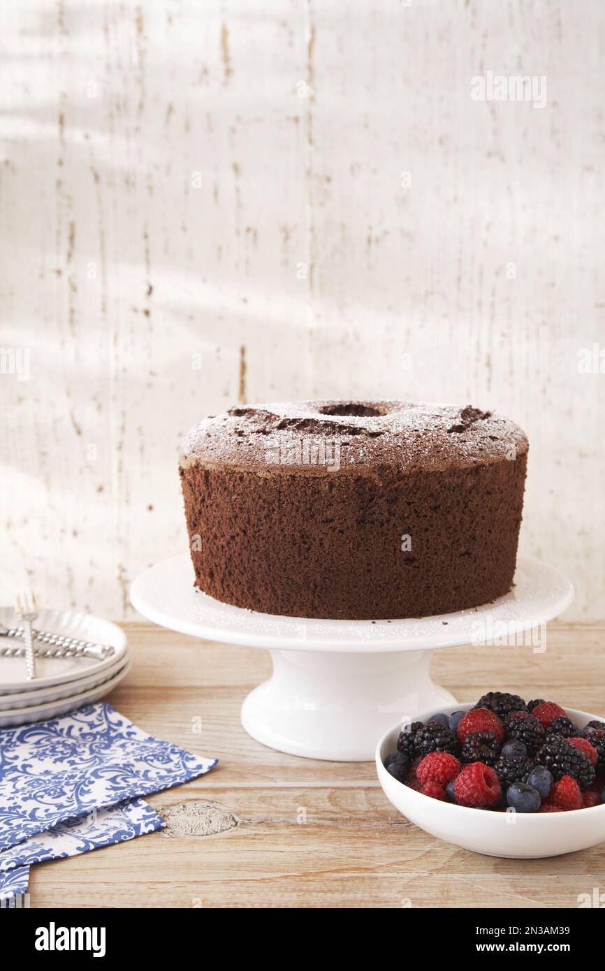 Chocolate cake with powdered sugar on a cake stand and a bowl of mixed berries to the side Stock Photo