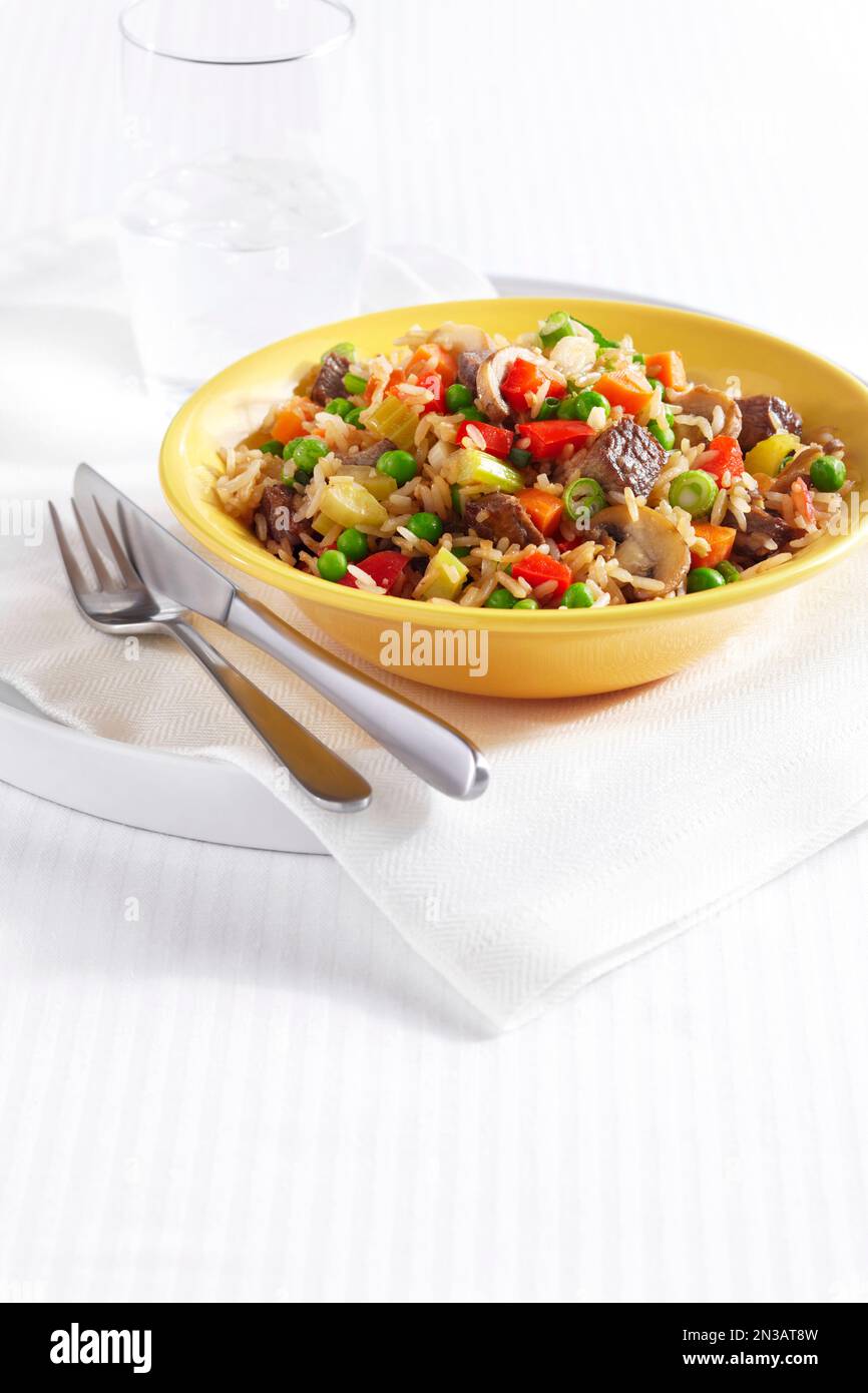 Fried Rice with pieces of beef, peppers, peas, celery, mushrooms and onion in a yellow bowl Stock Photo