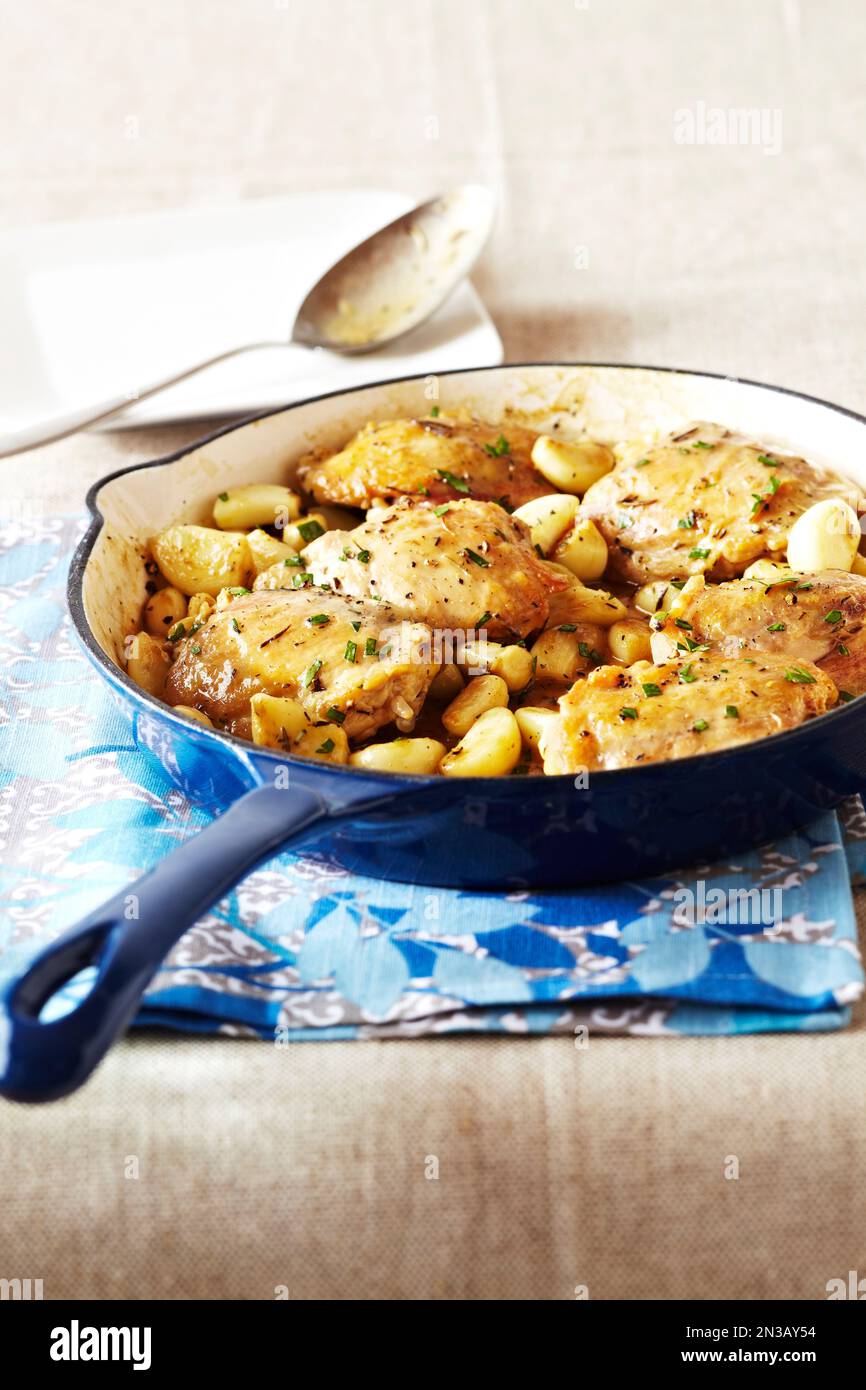 Blue skillet of chicken thighs with garlic on a patterned tea towel Stock Photo