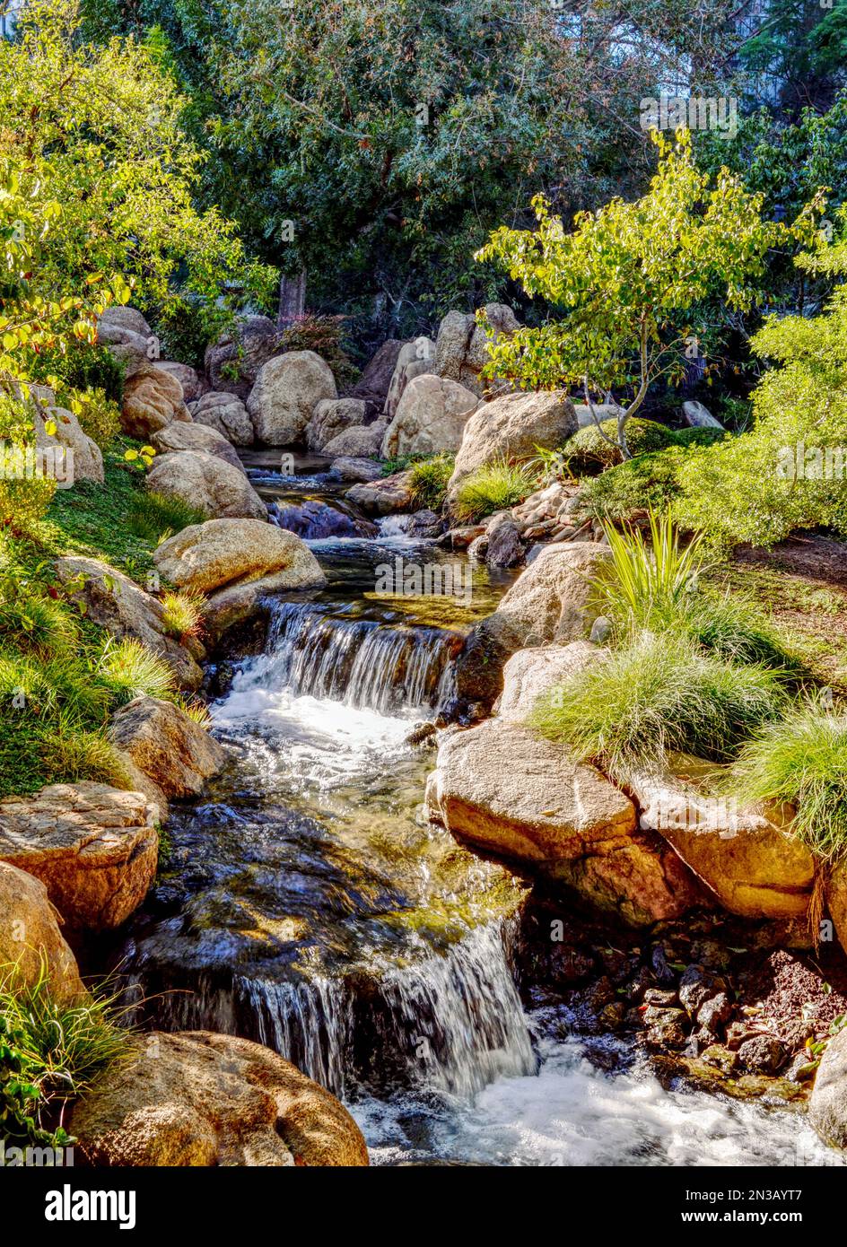 A vertical shot of a flowing rocky waterfall in a lush Japanese garden ...