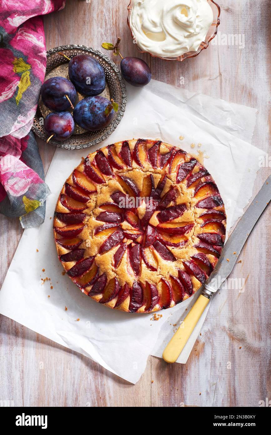 Plum cake with fresh plums and whipped cream and serving knife Stock Photo