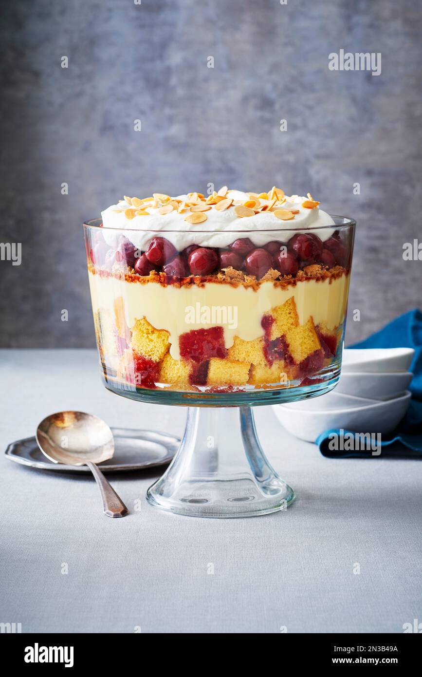 Cherry trifle in a glass trifle bowl with serving spoon on grey
