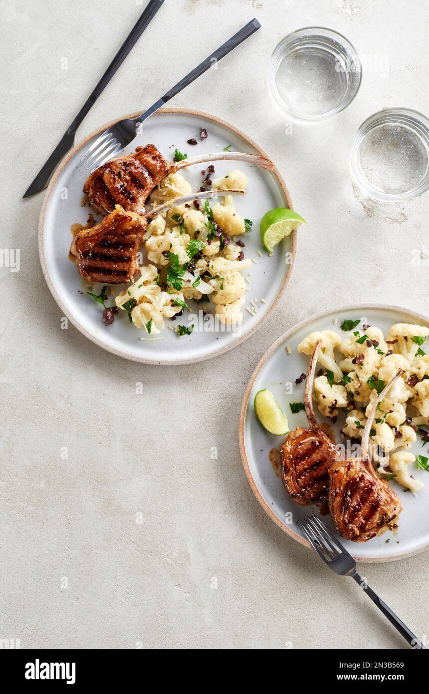 Two plates of grilled lamb chops with cauliflower salad on a grey