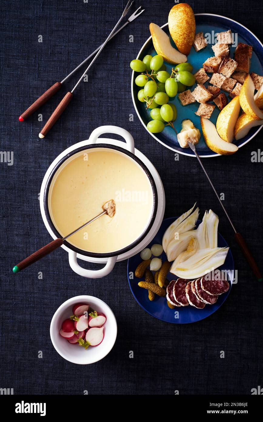 Cheese fondue with vegetables and fruit for dipping on a dark blue