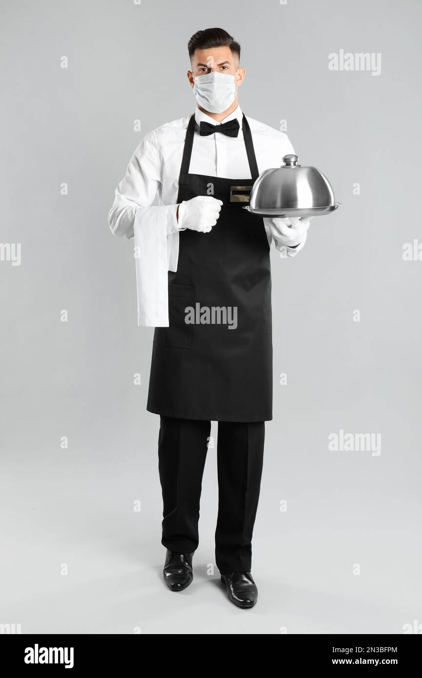 Waiter in medical face mask holding tray with lid on light grey ...