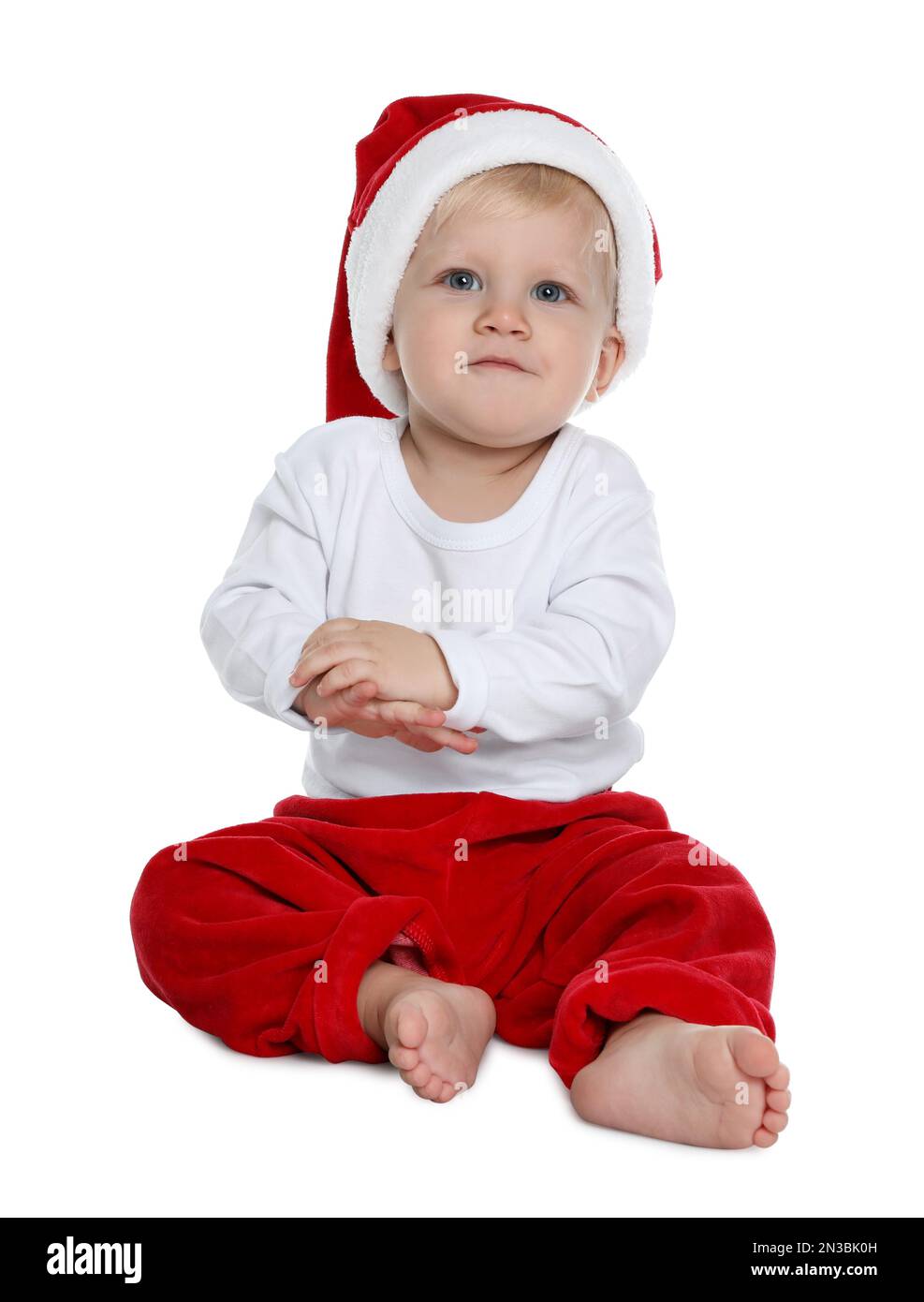 Cute baby in Santa hat and Christmas pajamas sitting on white