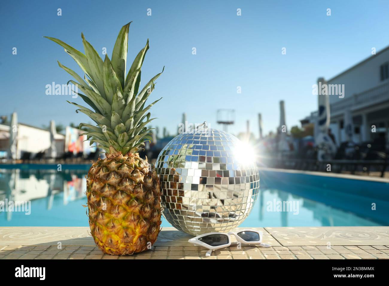 Shiny disco ball, pineapple and sunglasses on edge of swimming pool ...