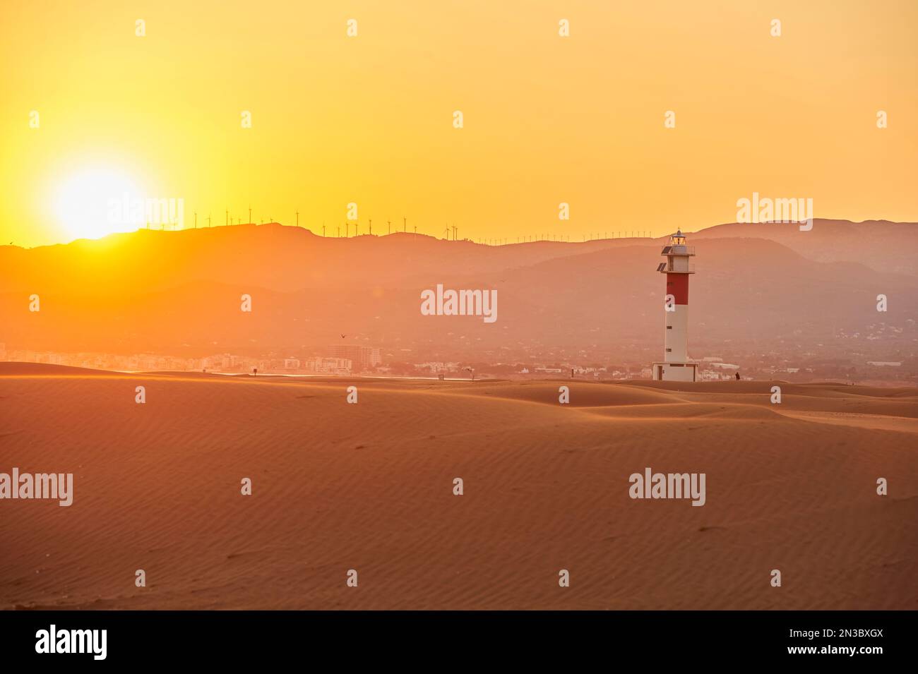 Lighthouse with red stripe on the rippled sand dunes in the evening light at sunset, Ebro River Delta; Catalonia, Spain Stock Photo